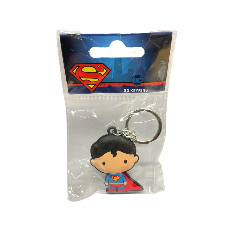 A keychain in a chibi style of a cartoon man with light skin and short dark hair that falls in a single curl over his forehead. He wears a blue costume with a red cape, red pants, red boots, and a yellow belt. A red and yellow symbol shaped like an S is on his chest.